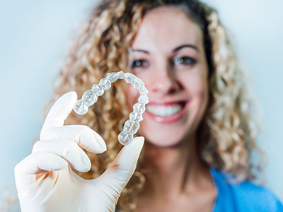 Woman in a lab coat holding up a transparent dental retainer.
