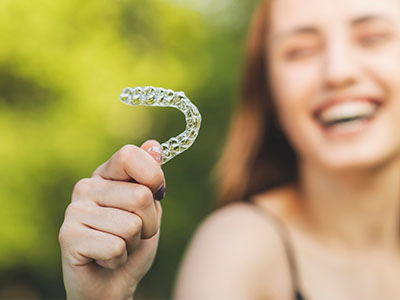 A smiling woman holding a transparent dental retainer.
