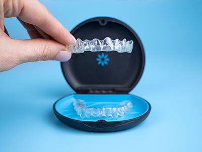 A human hand holding a clear plastic container displaying a set of transparent dental implants, with the brand name Invisalign visible on the top left corner.